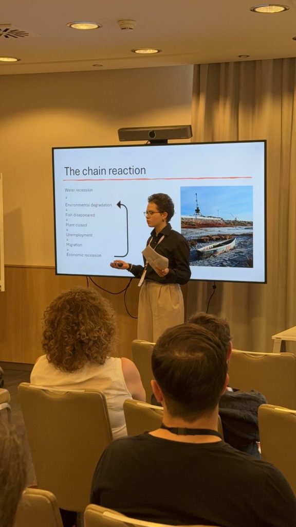 Presenter standing beside a projector screen labeled The chain reaction during a lecture